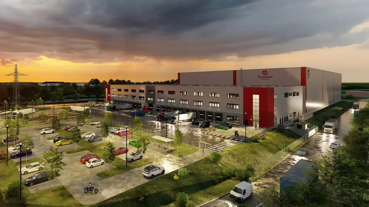 Visualisierung der Erweiterung des Queisser-Logistikzentrums bei Sonnenuntergang, mit beleuchtetem Parkplatz und Lieferfahrzeugen 