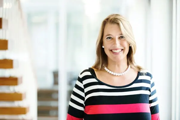 Lächelnde Frau mit Perlenkette vor heller Büro-Kulisse