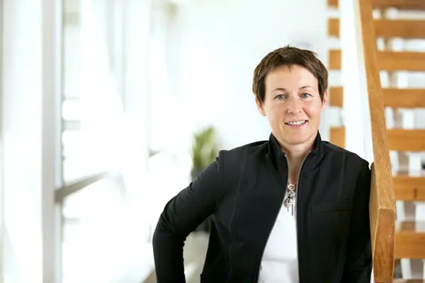 Frau mit kurzem Haar lehnt lächelnd an Holztreppe