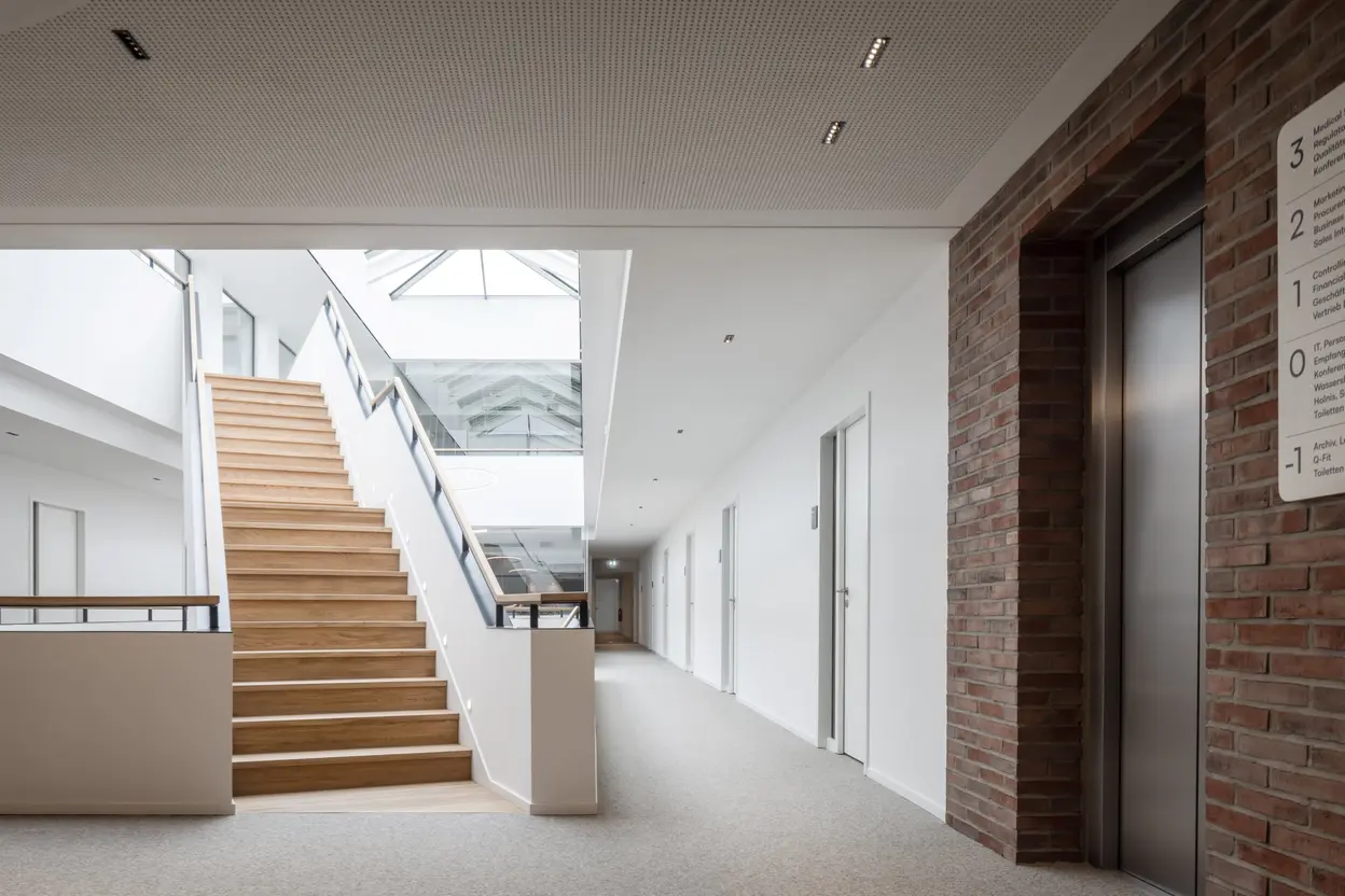 Innenansicht der Firmenzentrale von Queisser Pharma mit Holztreppe, gläsernem Dachlicht und Aufzug.