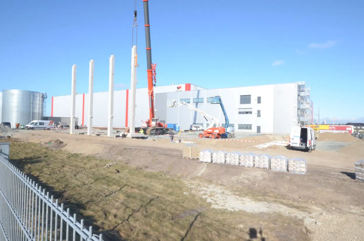 Bauarbeiten am Queisser-Logistikzentrum mit Hebekran, Arbeitsbühnen und errichteten Betonpfeilern vor dem Hauptgebäude.