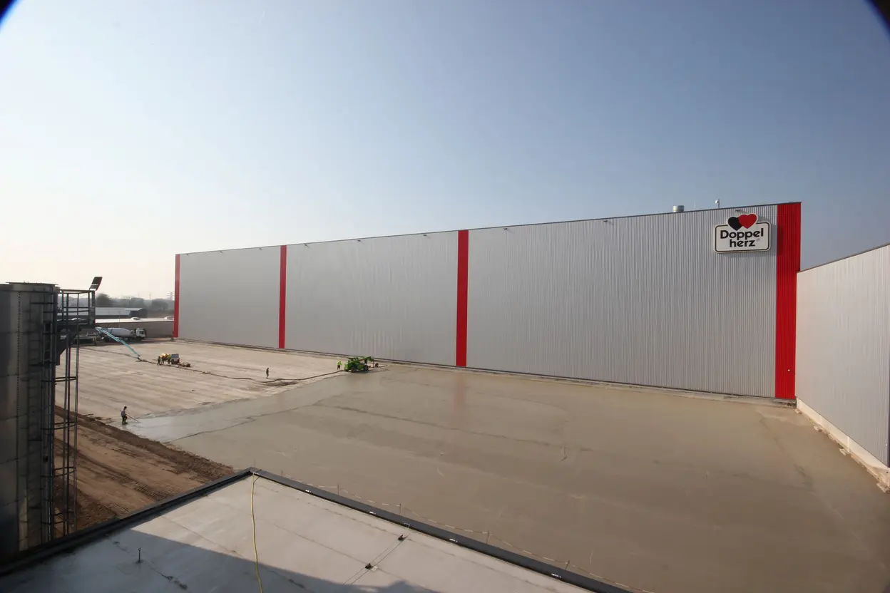 Aufbringen der Sauberkeitsschicht auf der Bodenplatte vor dem Queisser-Logistikzentrum mit Doppelherz-Logo, Arbeitsgeräte im Einsatz