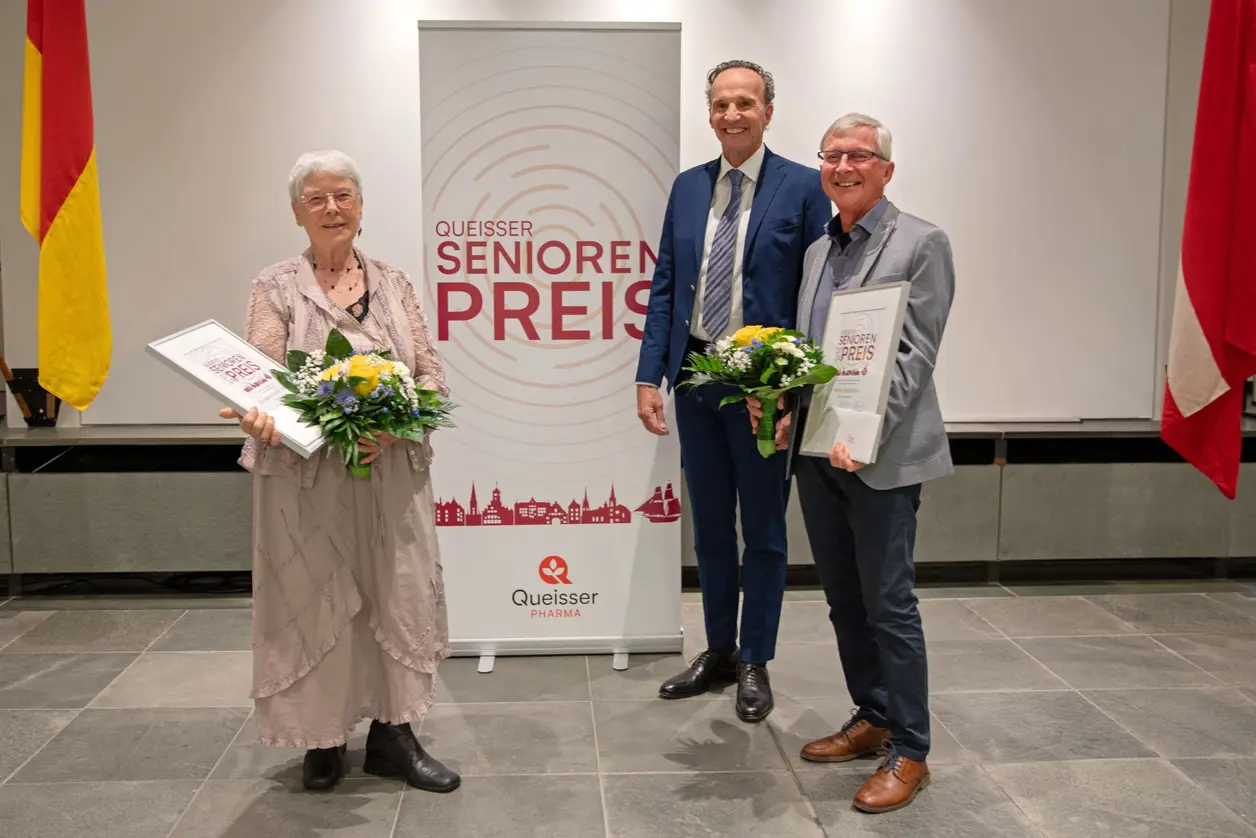 Geschäftsführer Erich Nobis mit den beiden Preisträger*innen des Queisser Seniorenpreises 2024 vor einem Roll-Up mit dem Schriftzug "Queisser Senorenpreis"