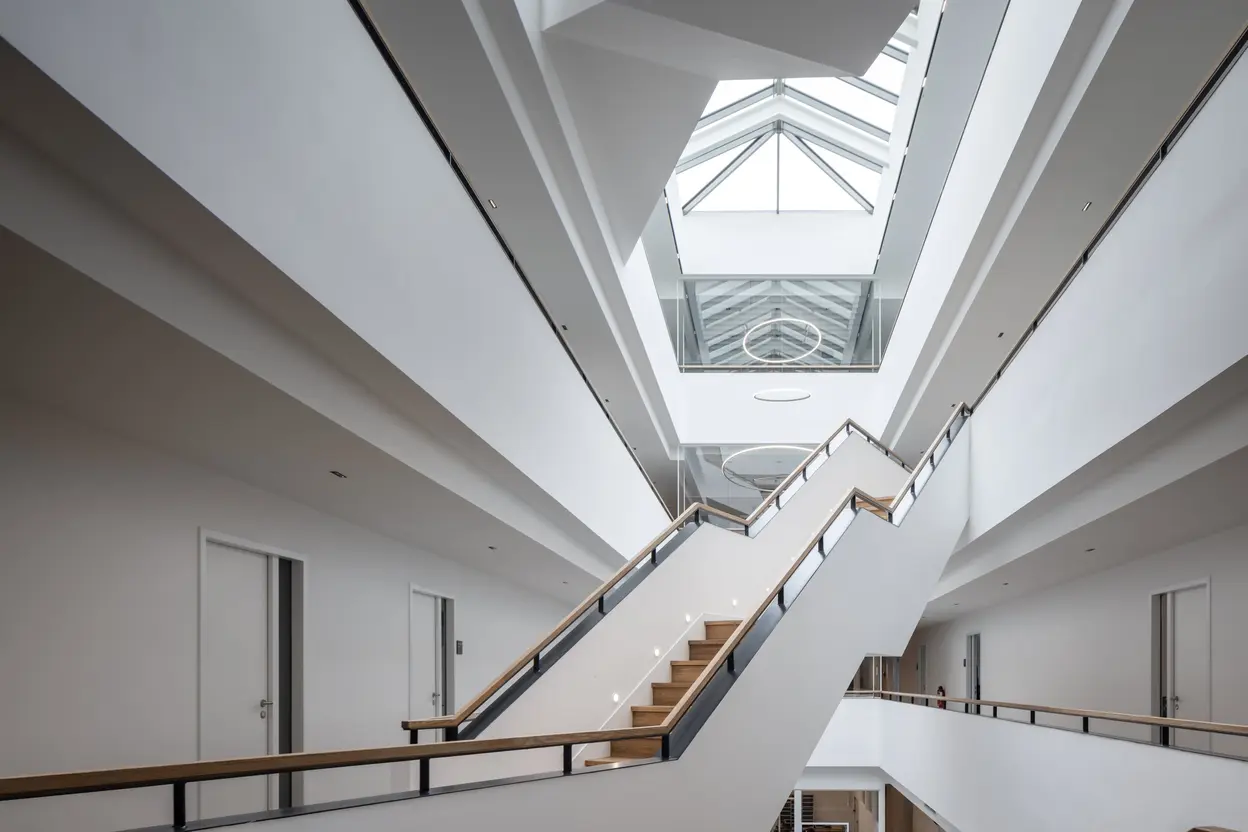 Atrium mit freitragender Treppe, weißem Geländer und Glasdach