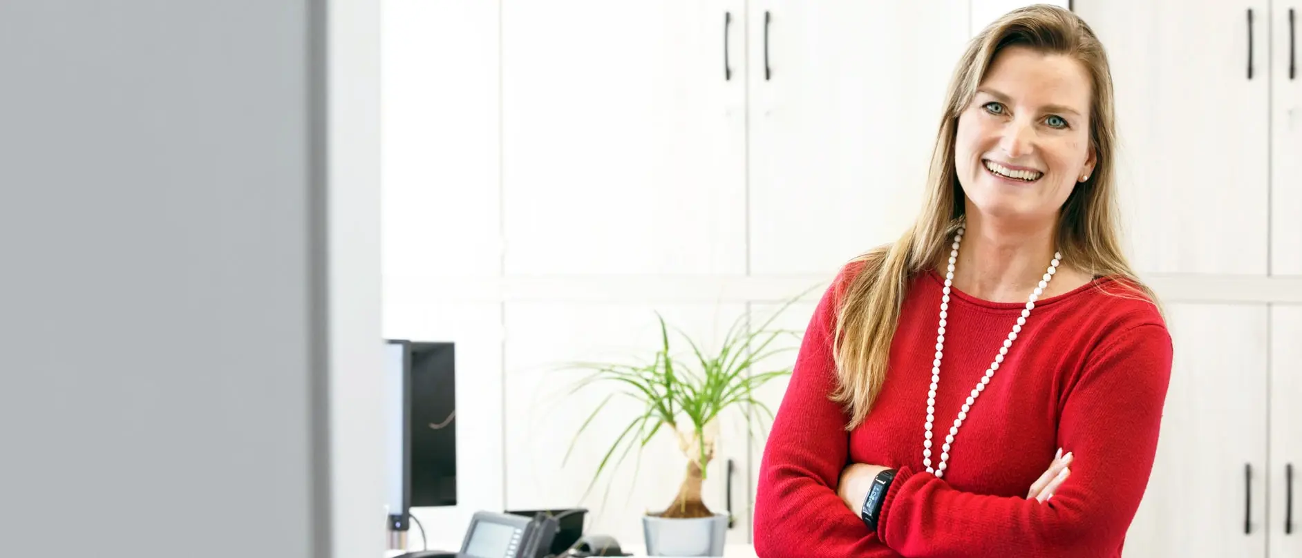 Frau im roten Pullover steht lächelnd im Büro