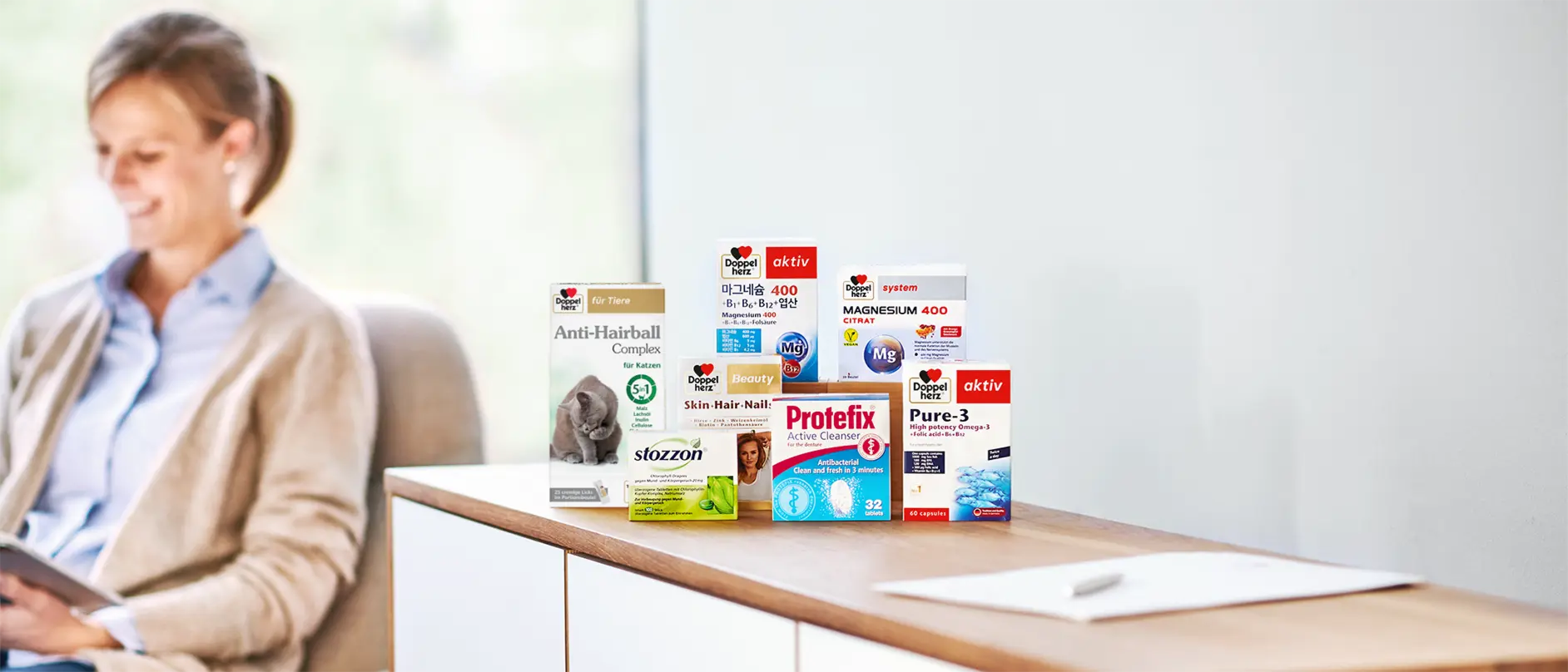 Queisser-Produkte auf einem Sideboard, im Hintergrund sitzt eine lächelnde Frau.