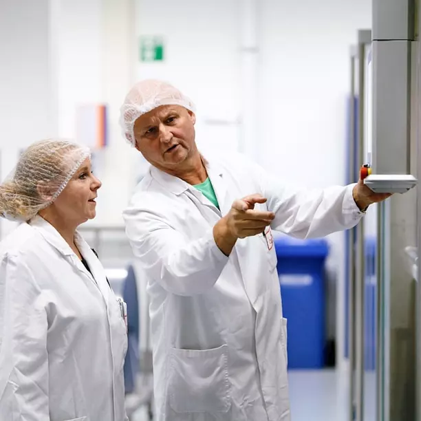 Ein Mitarbeiter und eine Mitarbeiterin in Laborkleidung in einer Gesprächssituation