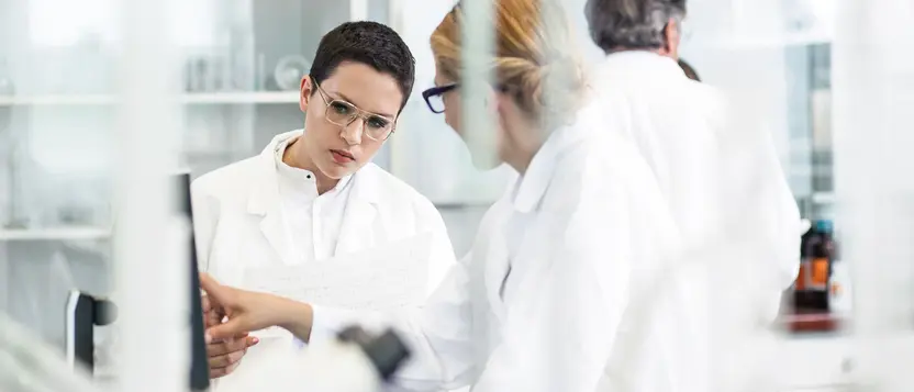 Zwei Personen im Labor besprechen Daten, beide tragen Laborkittel.