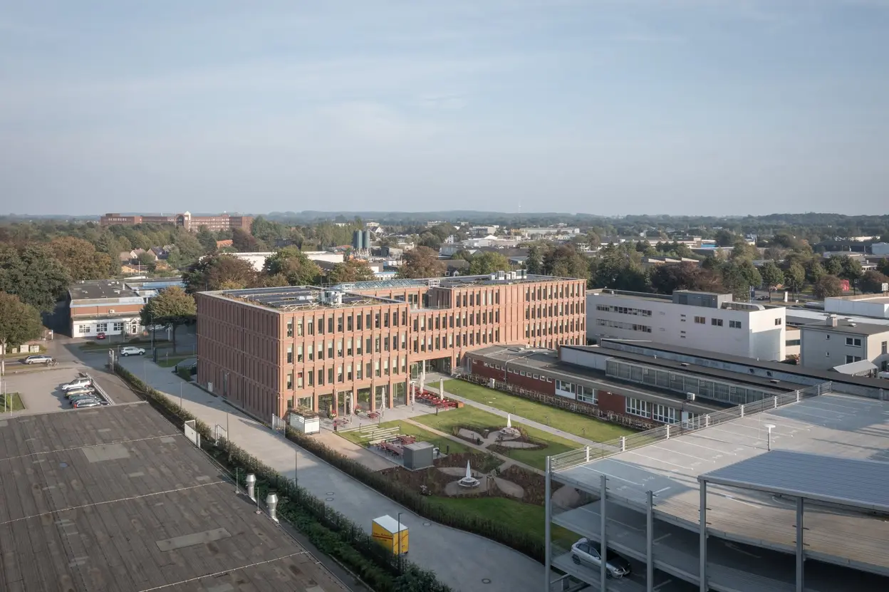 Luftaufnahme des Queisser-Campus mit modernem Verwaltungsgebäude, begrüntem Innenhof und Parkhaus im Vordergrund.