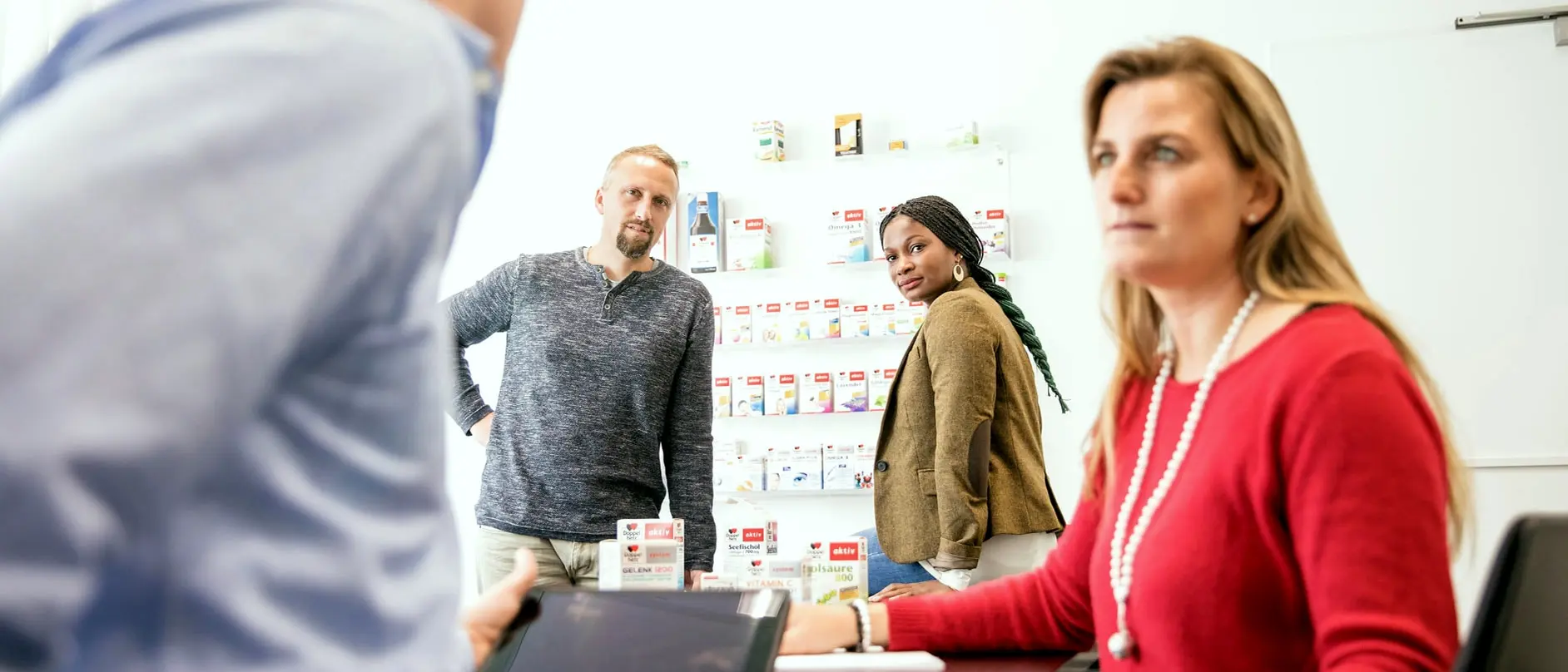 „Vier Personen im Gespräch in einem modernen Büro, Fokus auf eine Frau im roten Pullover