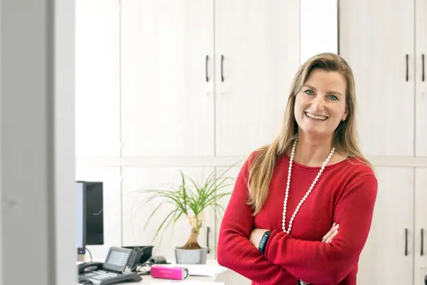 Frau im roten Pullover steht lächelnd im Büro