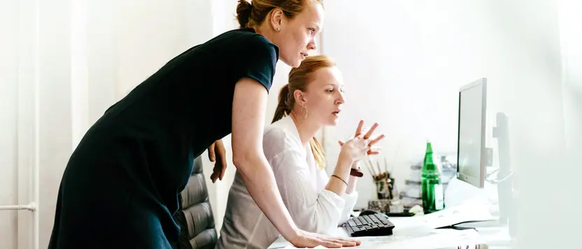 Zwei Mitarbeiterinnen schauen gemeinsam auf einen Bildschirm am Schreibtisch