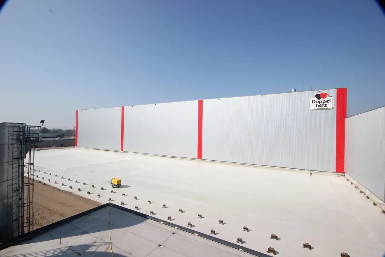 Fertiggestellte Betonfläche vor der Hallenfassade des Queisser-Logistikzentrums mit Doppelherz-Logo und roten Streifen, bei klarem Himmel.