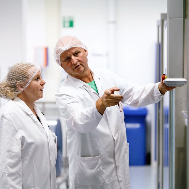 Ein Mitarbeiter und eine Mitarbeiterin in Laborkleidung in einer Gesprächssituation